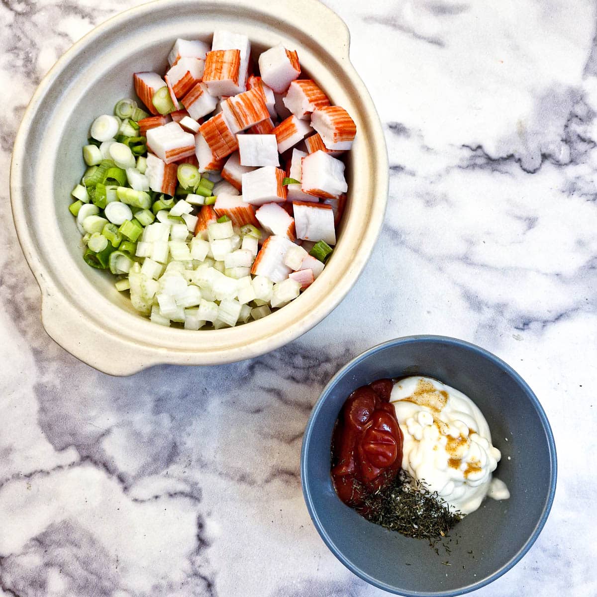 Chopped crab sticks, spring onions and celery in one bowl with mayonnaise, tomato ketchup, dill and tabasco in another bowl.