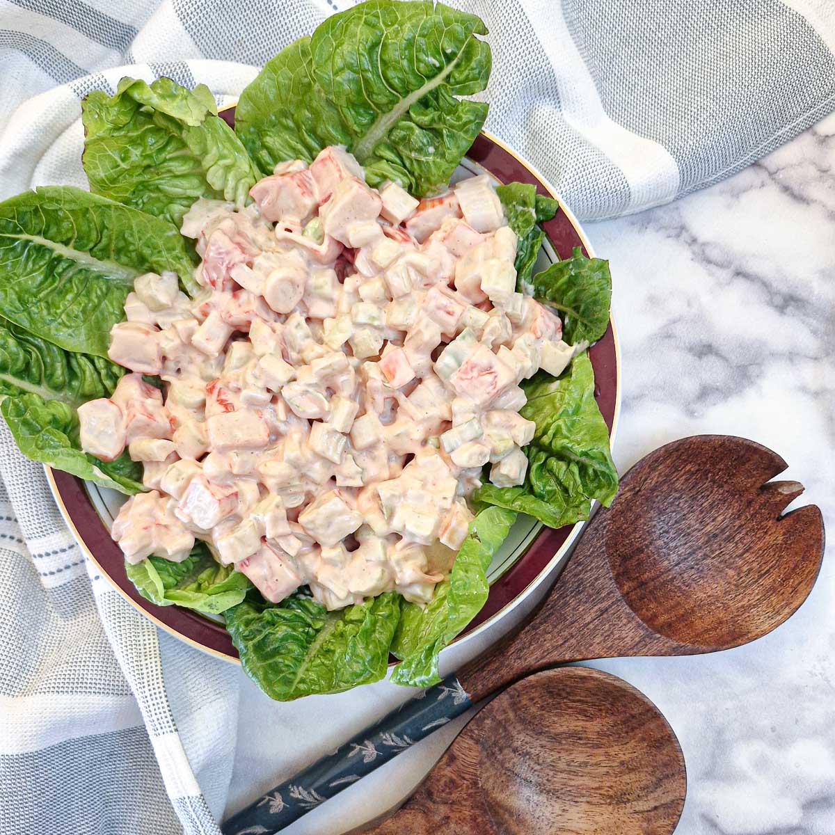 Imitation crab salad starter on a bed of lettuce.  There are 2 wooden serving spoons in the foreground.