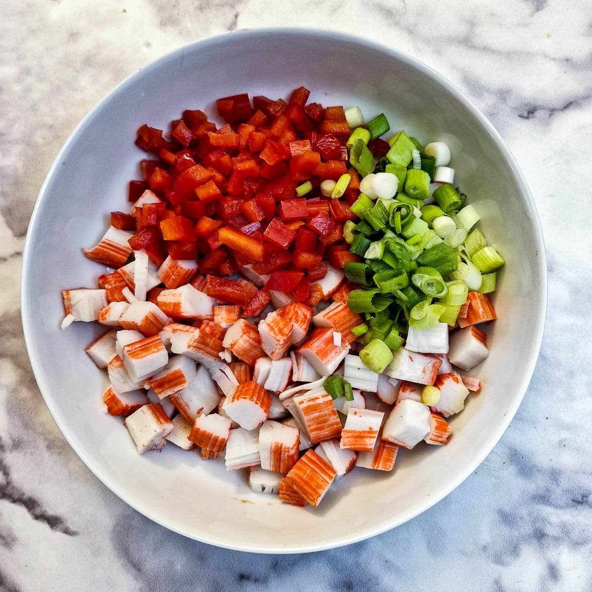Chopped red pepper, spring onions and crab sticks in a white bowl.