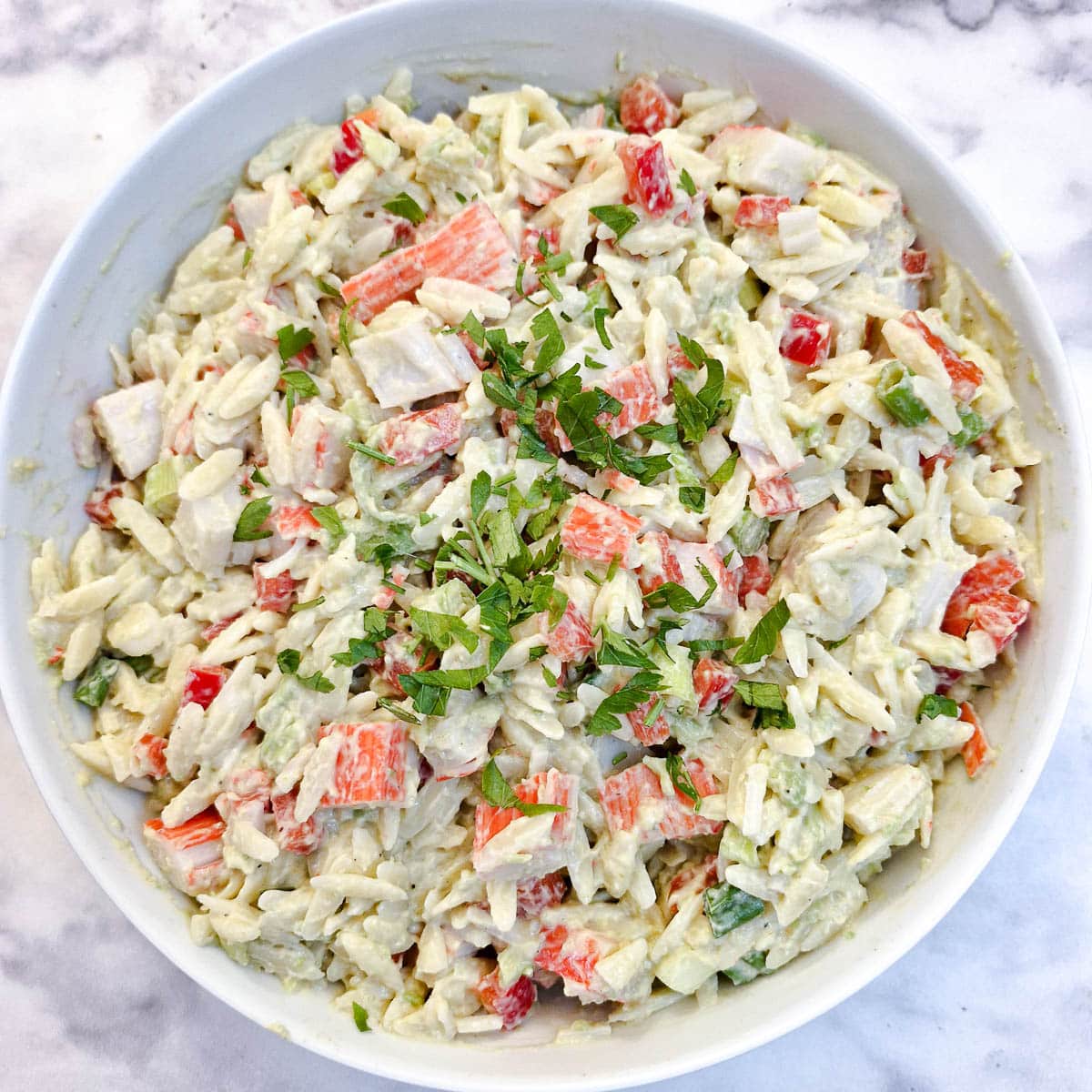 Overhead shot of imitation crab pasta salad garnished with parsley.