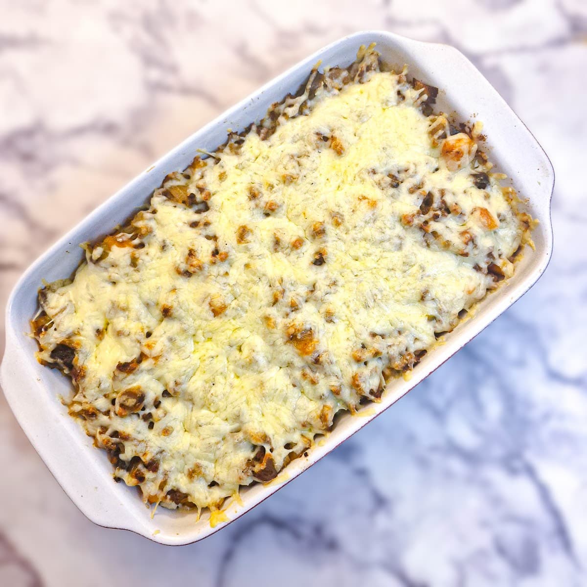 Overhead shot of a baked dish of mince and potato bake with melted cheese on top.