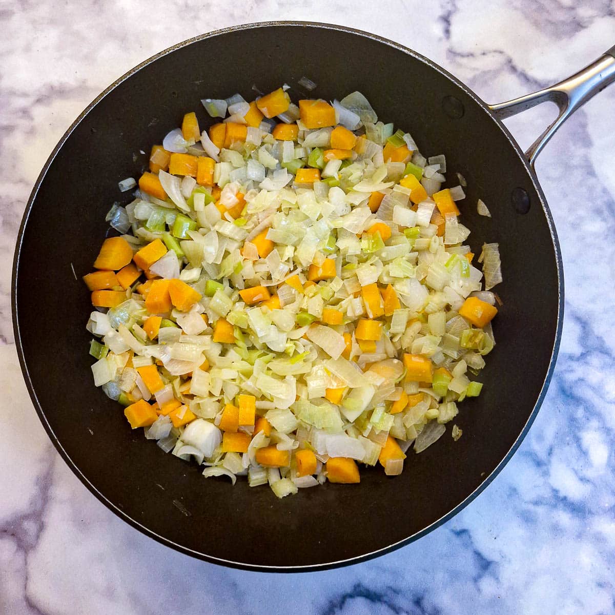 Finely chopped carrots, onions and leeks in a frying pan.