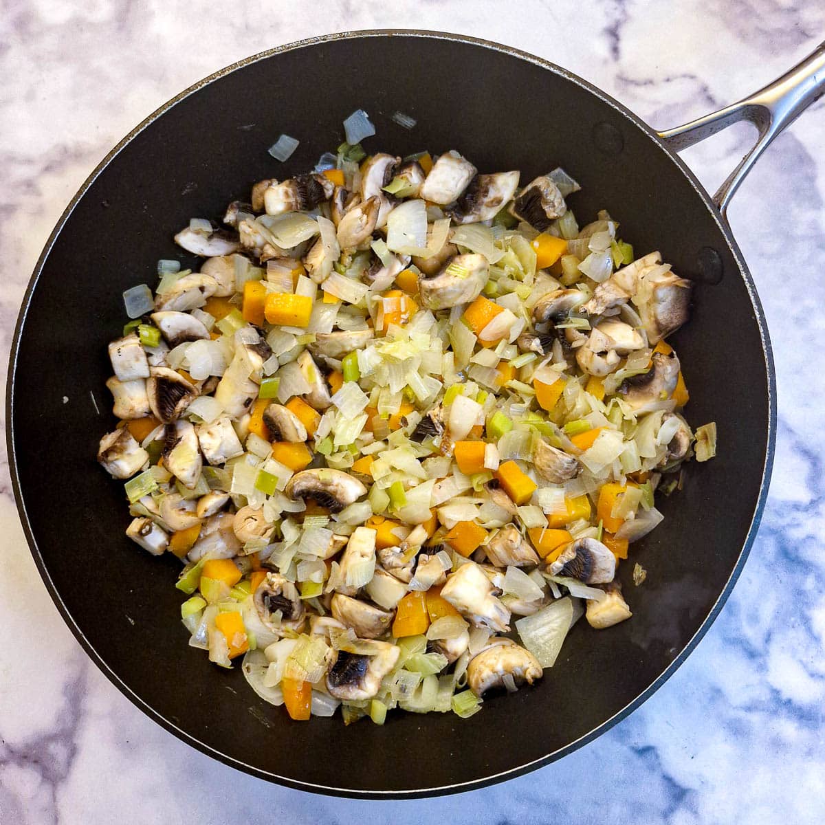 Mushrooms frying with vegetables in a frying pan.