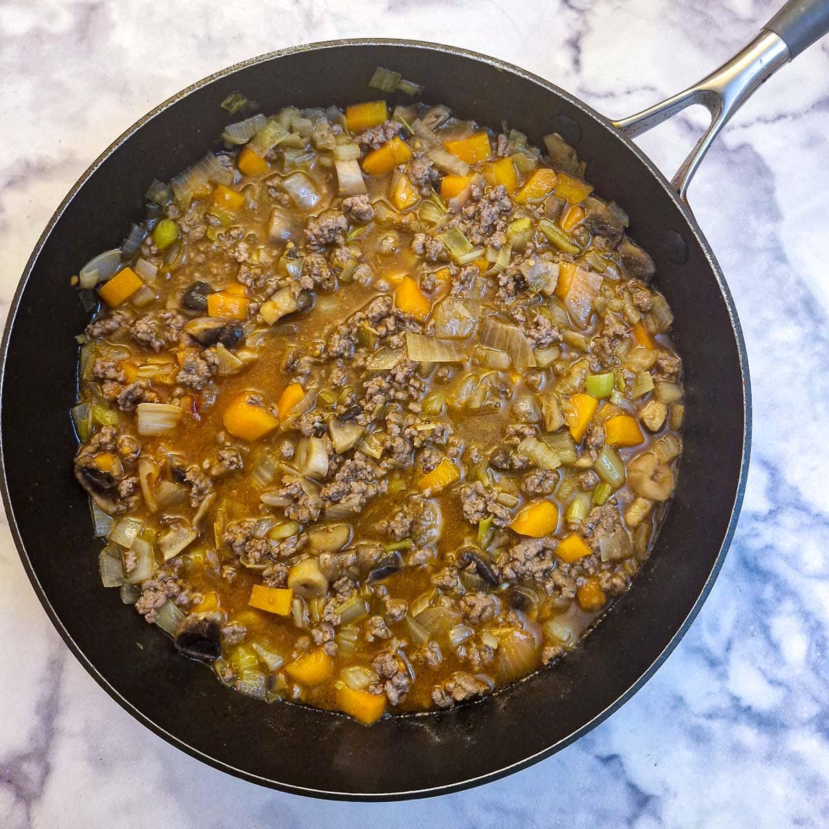 A frying pan containing beef mince and vegetables in stock.