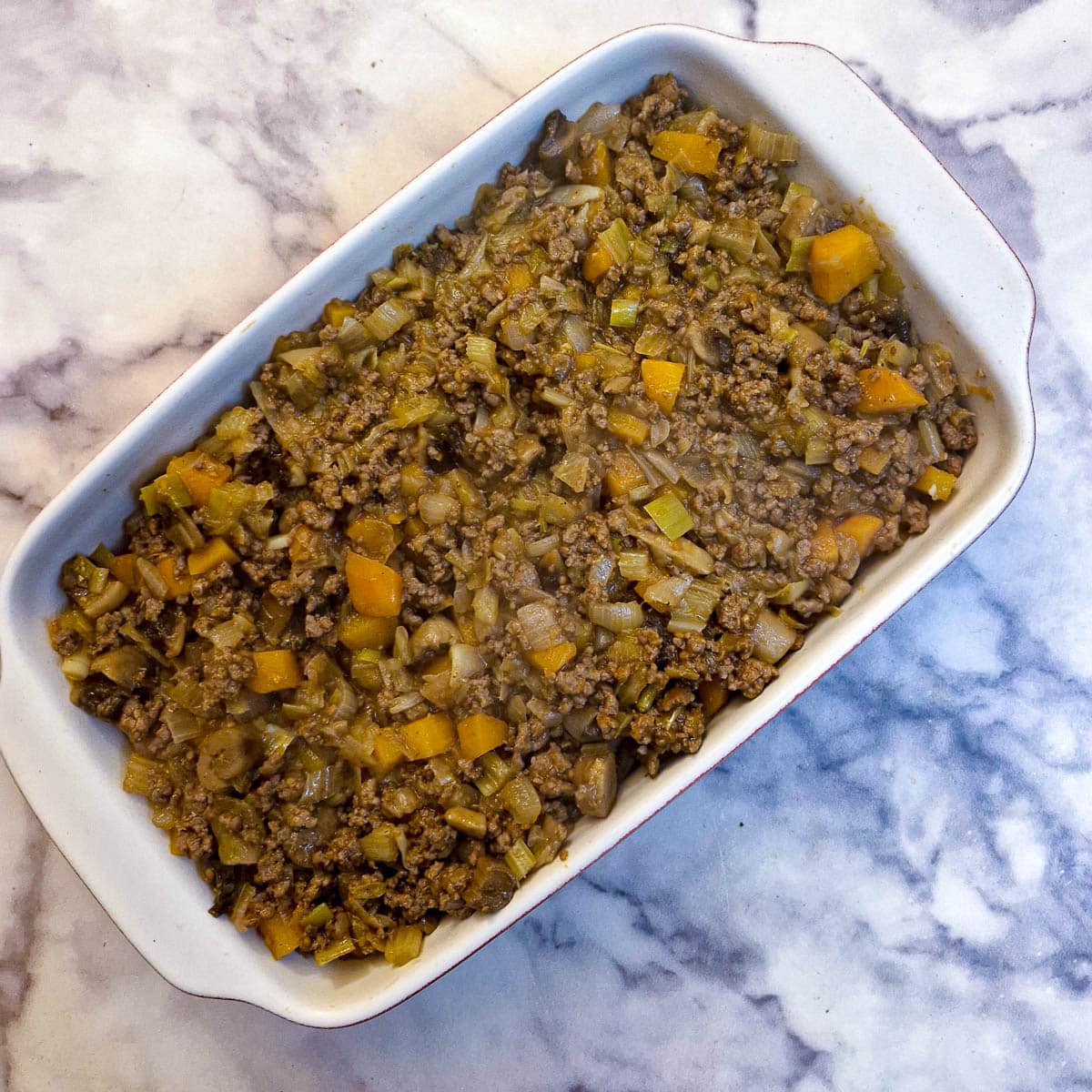 Mince mixture poured on top of potatoes in a casserole dish.