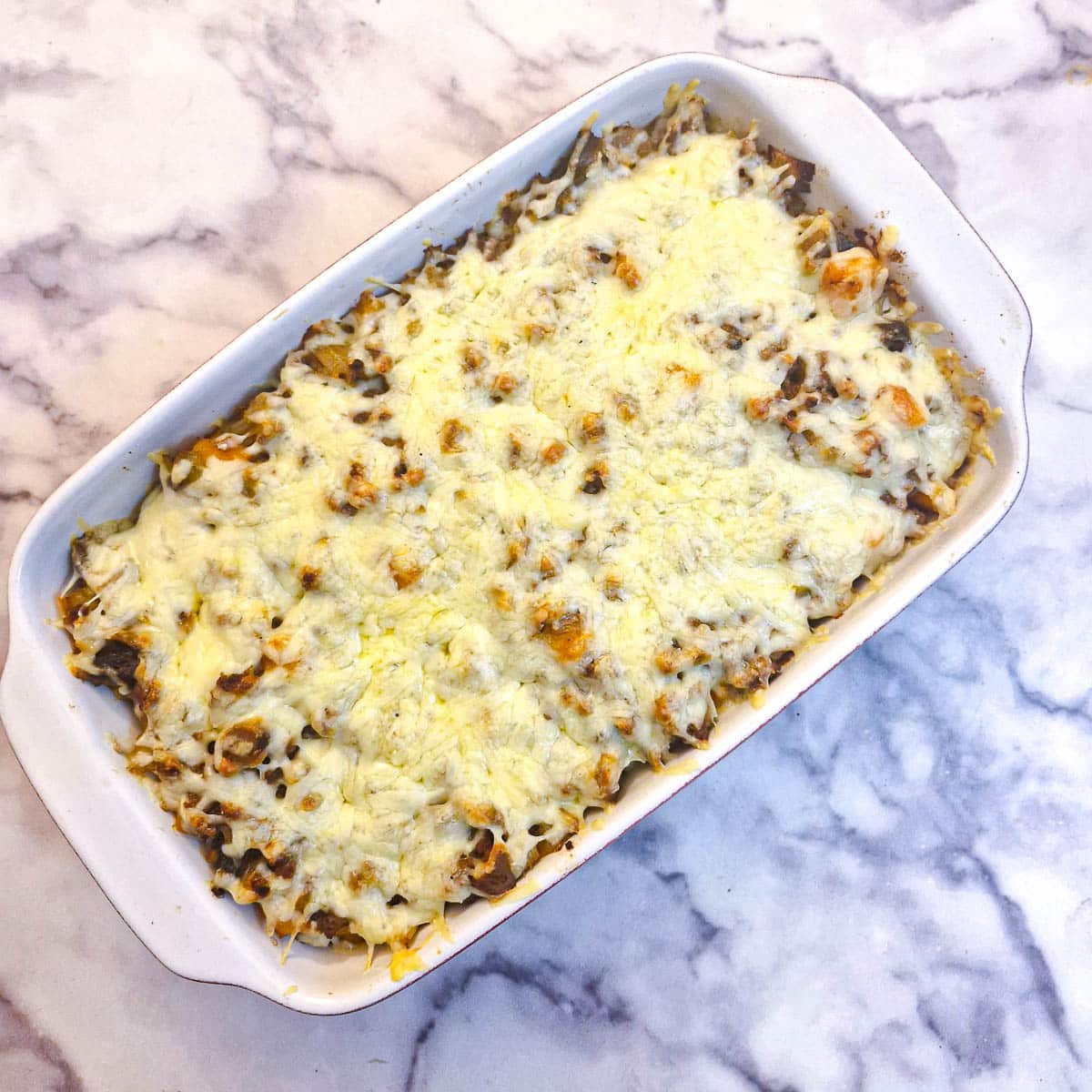 A baked dish of mince and potato bake with melted cheese on top.