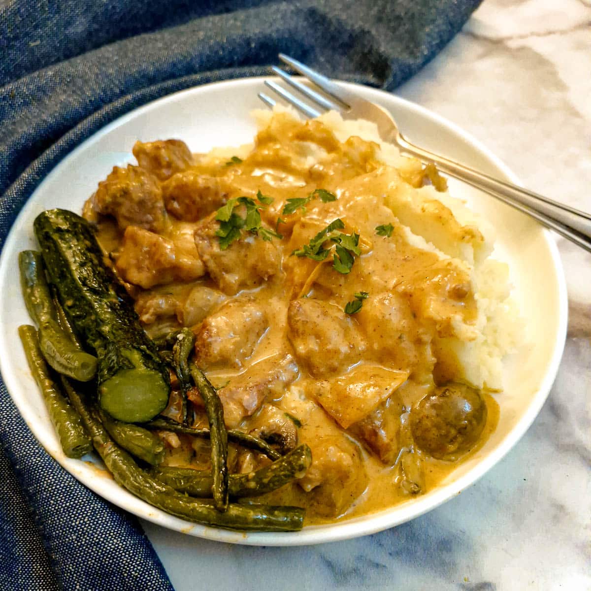 Creamy paprika pork goulash on a white plate with green vegetables.