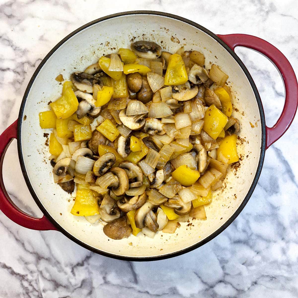 Yellow capsicum, onions and mushrooms frying in a casserole dish.