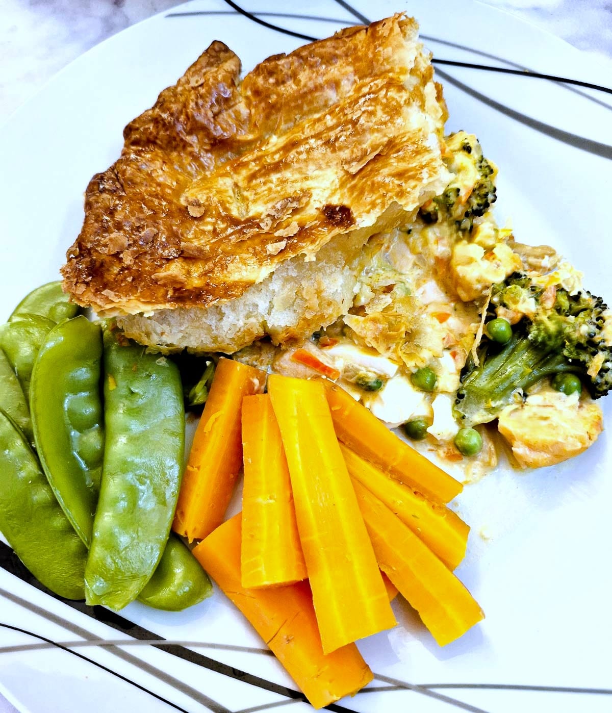 A s;lice of salmon and red pepper pie on a plate with mange tout and carrots.