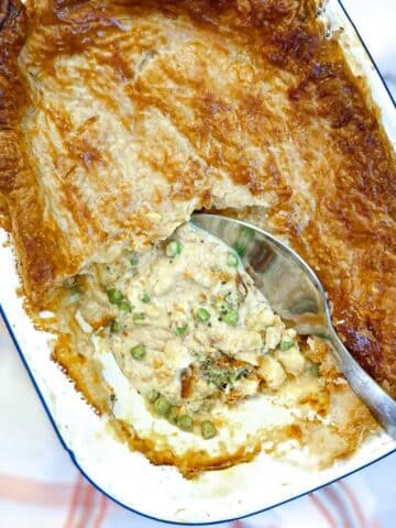 A white baking dish containing a salmon and red pepper sauce pie with the corner removed to show the filling.