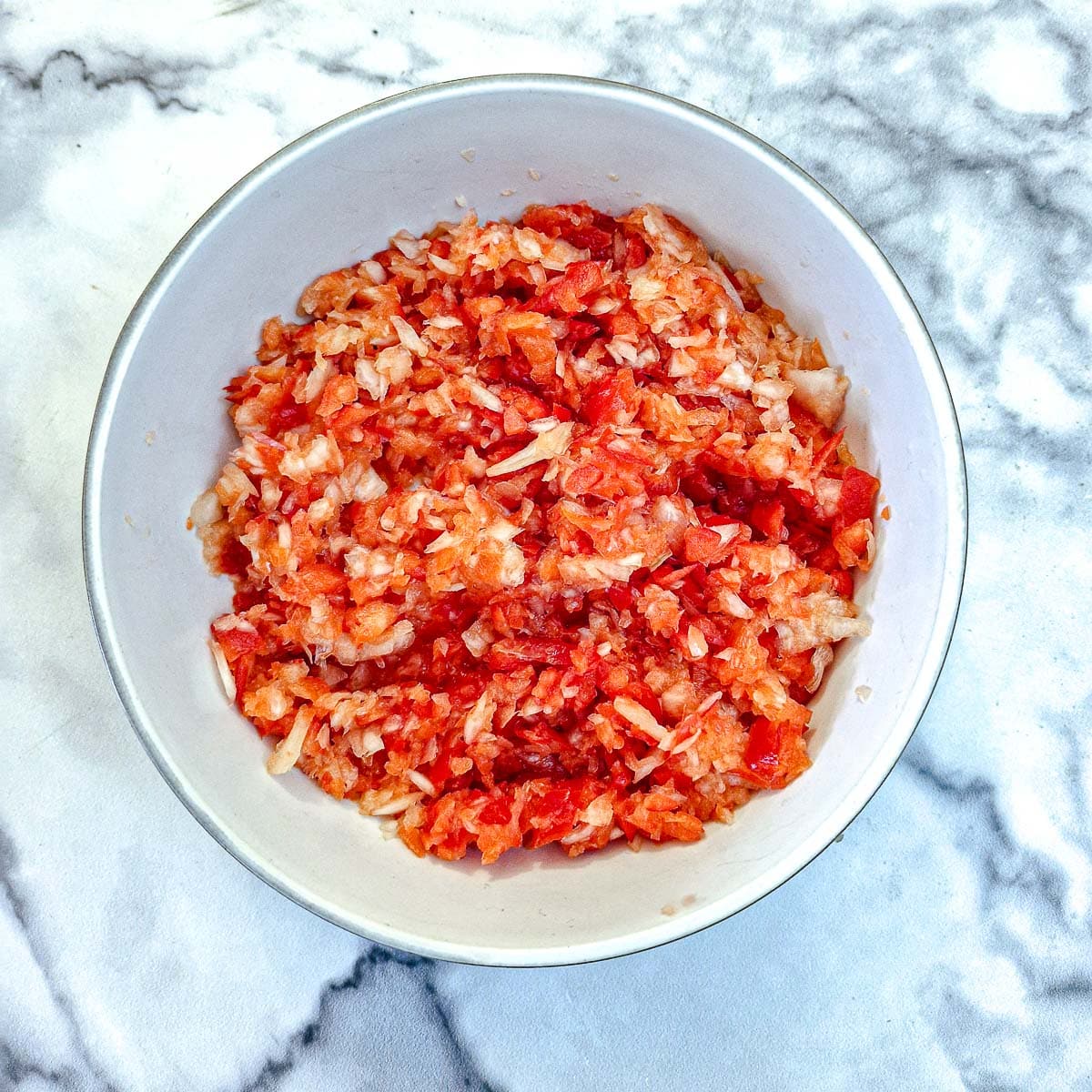 Finely chopped red peppers and onions in a whit bowl.