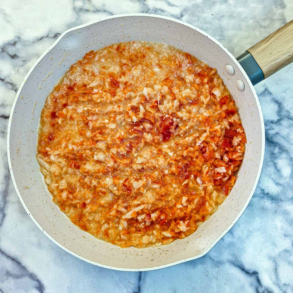 Red peppers and onions softening in a frying pan.