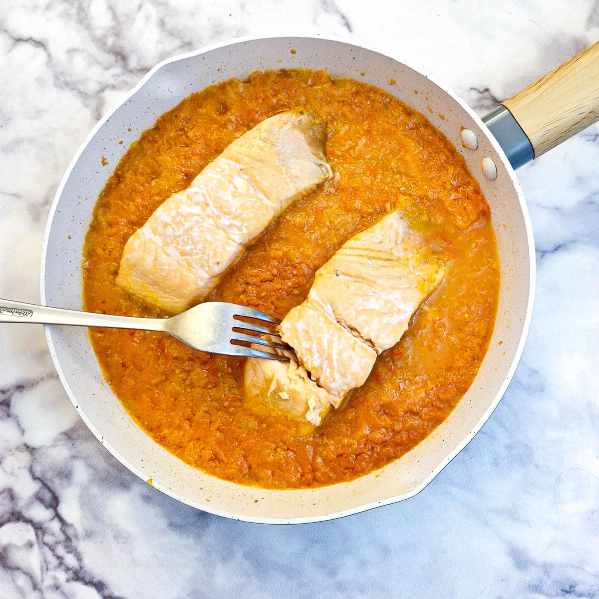 Poached salmon fillets being flaked with a fork.