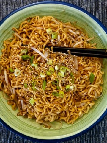 A green serving dish of Chinese noodles with a pair of black chopsticks.