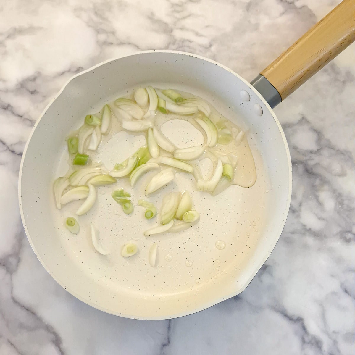 Chopped onions and spring onions in a frying pan.