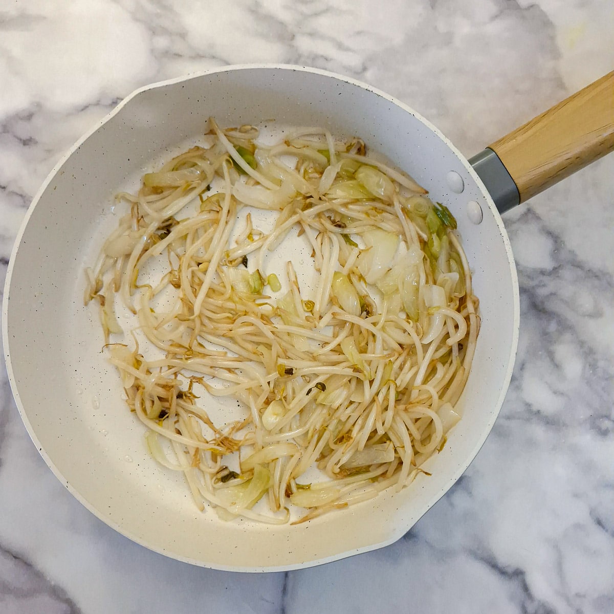 Beansprouts added to onions in a frying pan.