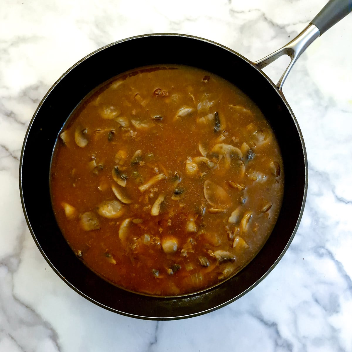 Stock, onions, mushrooms and fried ground beef in a frying pan.