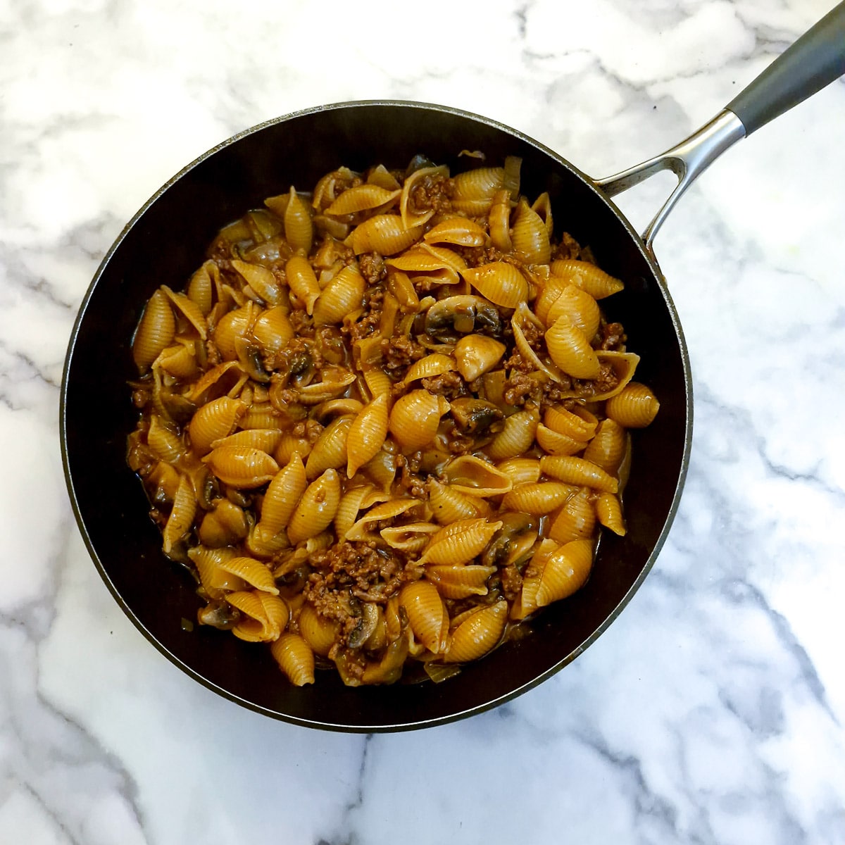 A dish of softened pasta with ground beef, onions and mushrooms.