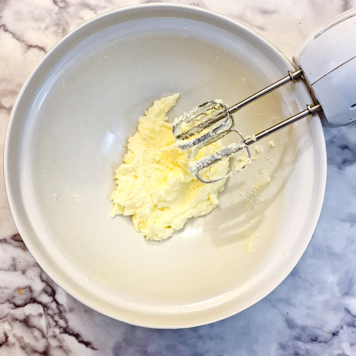 Creamed butter and sugar in a mixing bowl with a hand-held electric mixer.