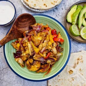 A green serving dish filled with oven-baked chicken fajitas.