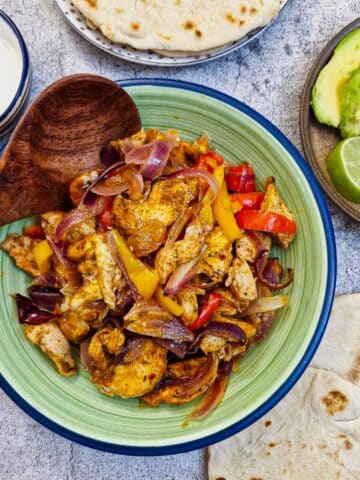 A green serving dish filled with oven-baked chicken fajitas.