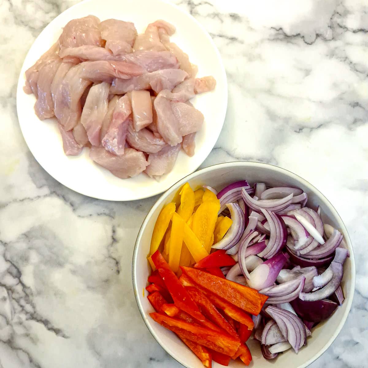 Sliced chicken and slices of capsicum and onions in two dishes.