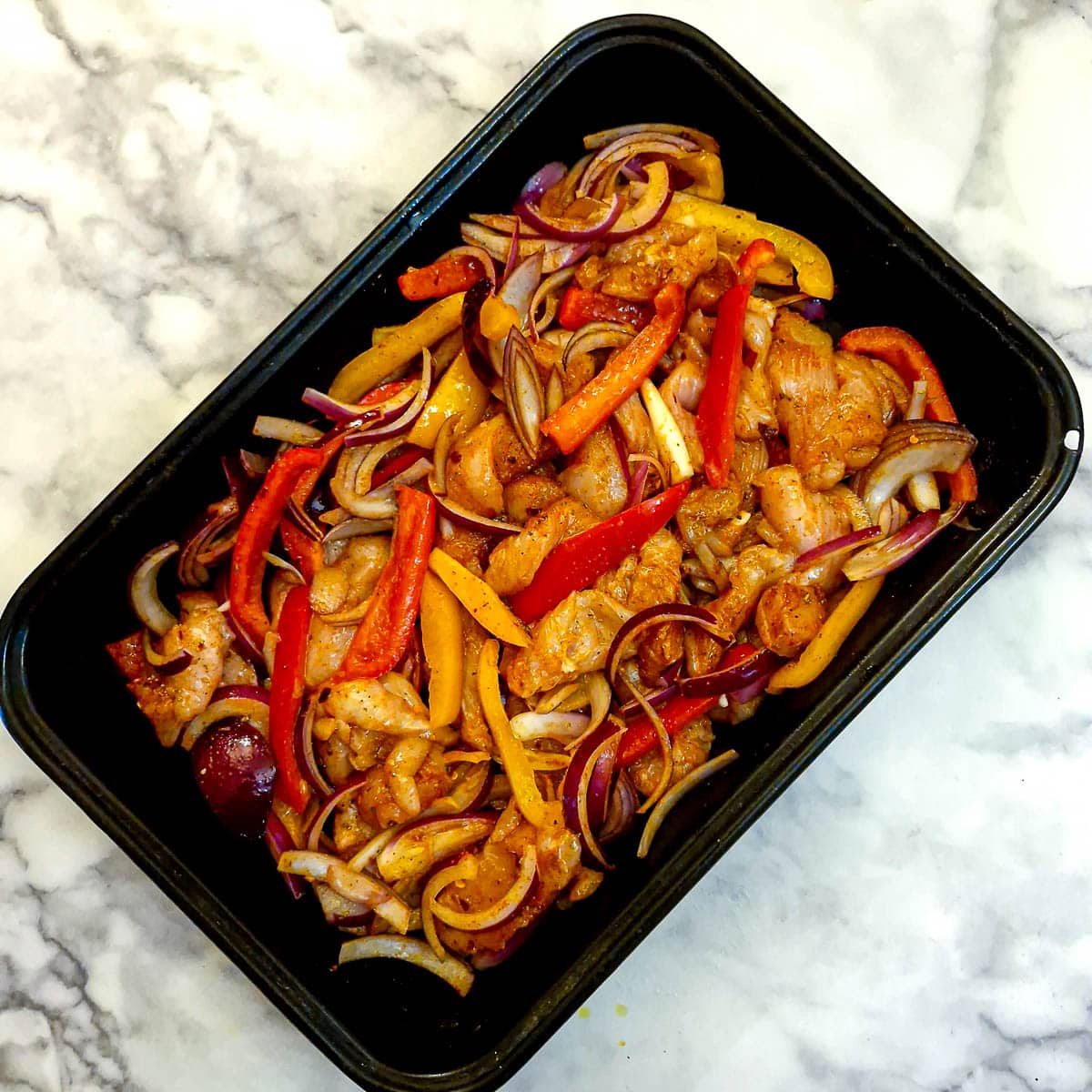 Raw chicken strips, onions and sliced peppers arranged in a baking dish.