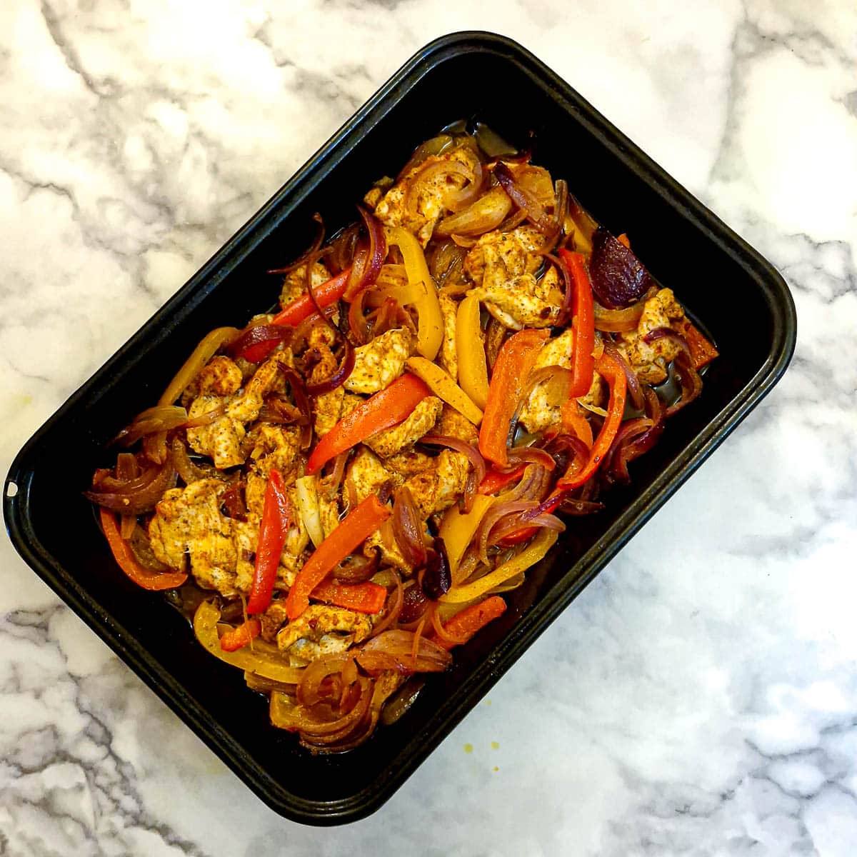 Cooked chicken strips, onions and sliced peppers arranged in a baking dish.