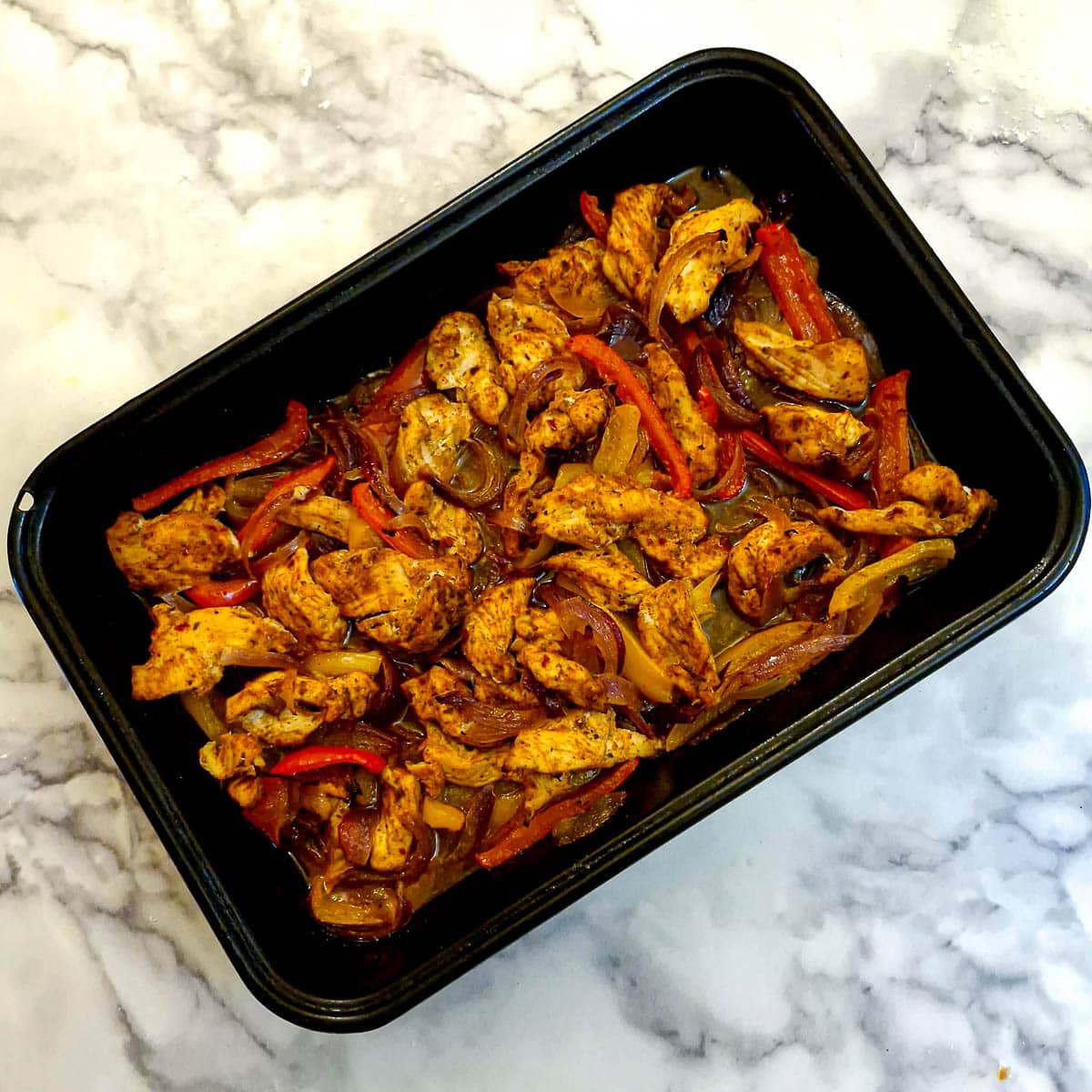 Lightly browned cooked chicken strips, onions and sliced peppers arranged in a baking dish.