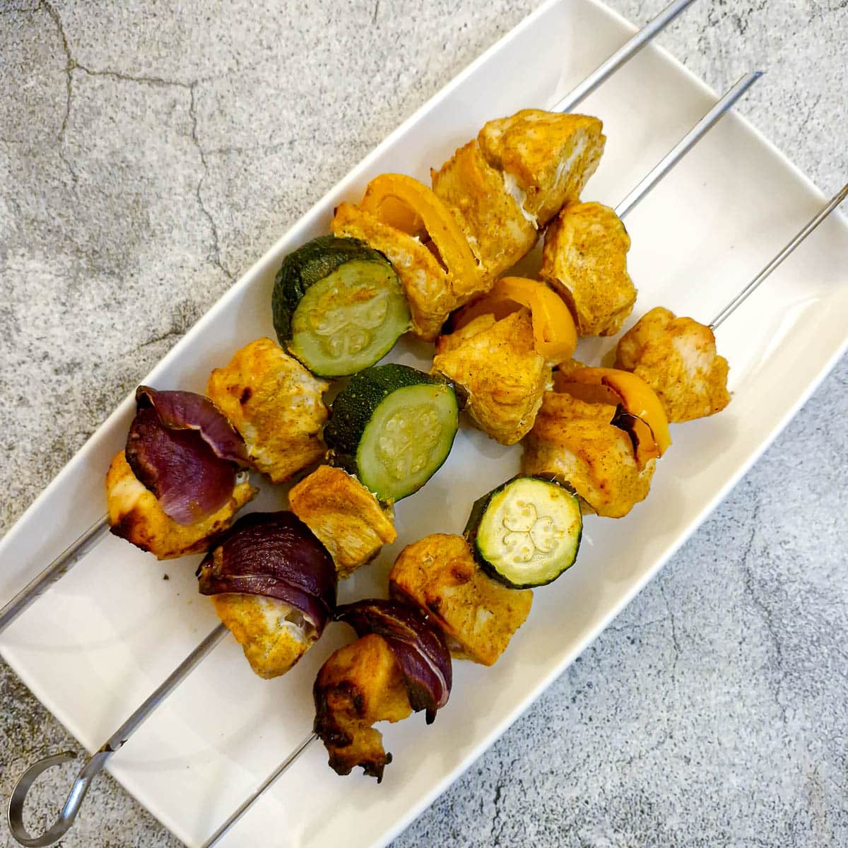 Three chicken skewers on a long white platter.