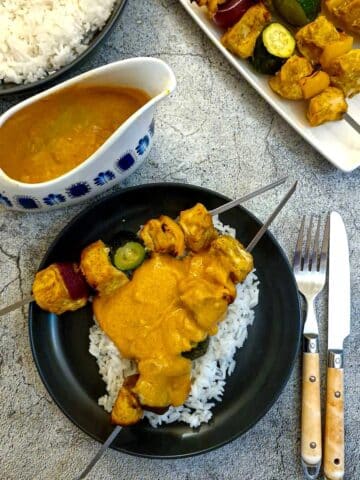 Two chicken tikka skewers on a bed of rice, smothered in creamy tikka sauce.