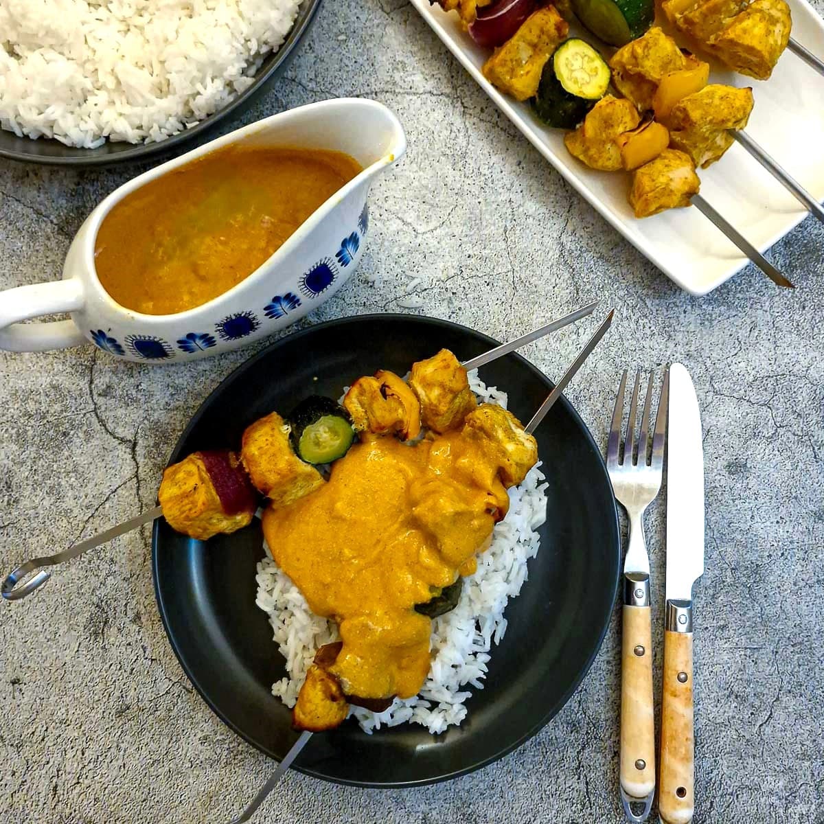 Two chicken tikka skewers on a bed of rice, smothered in creamy tikka sauce.