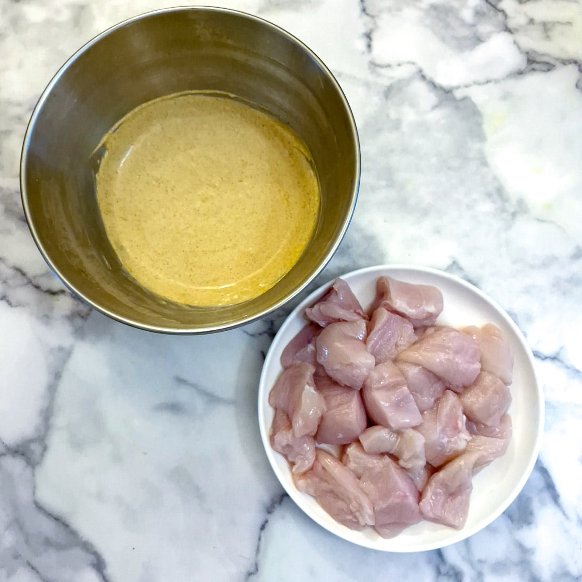 A small mixing bowl containing marinade ingredients and a plate of chopped up chicken pieces.