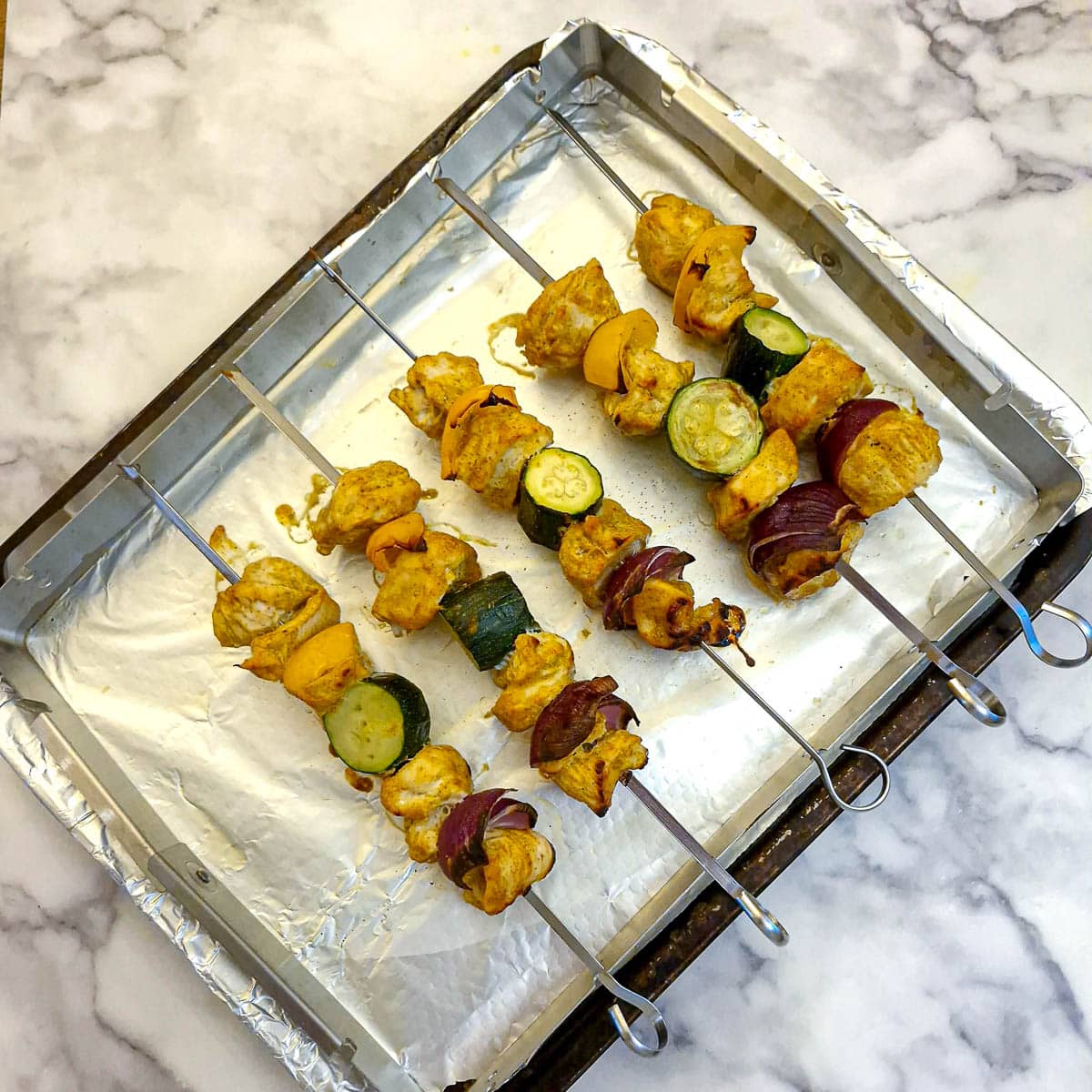 5 cooked chicken skewers on a metal rack.