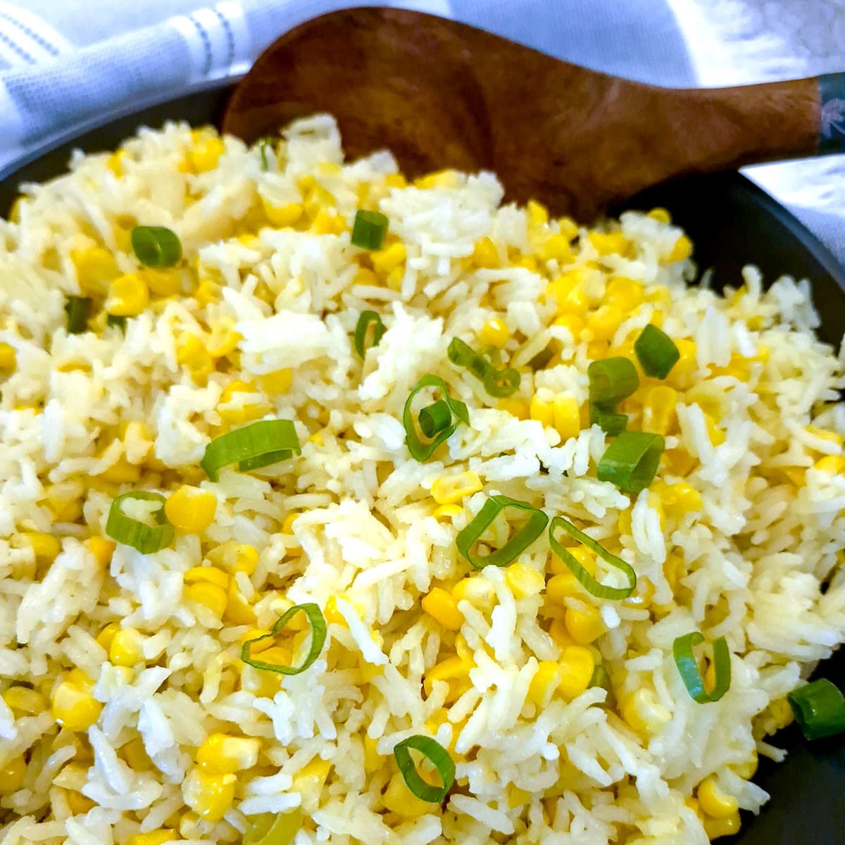 Closeup of a dish of buttered corn and rice garnished with green onions,