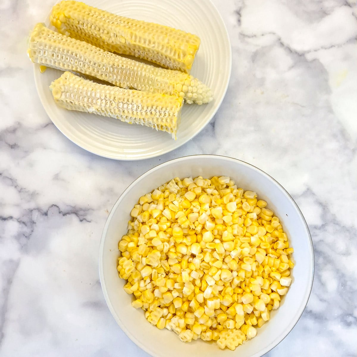 A dish of freshly cut corn kernels with the cobs in the background.