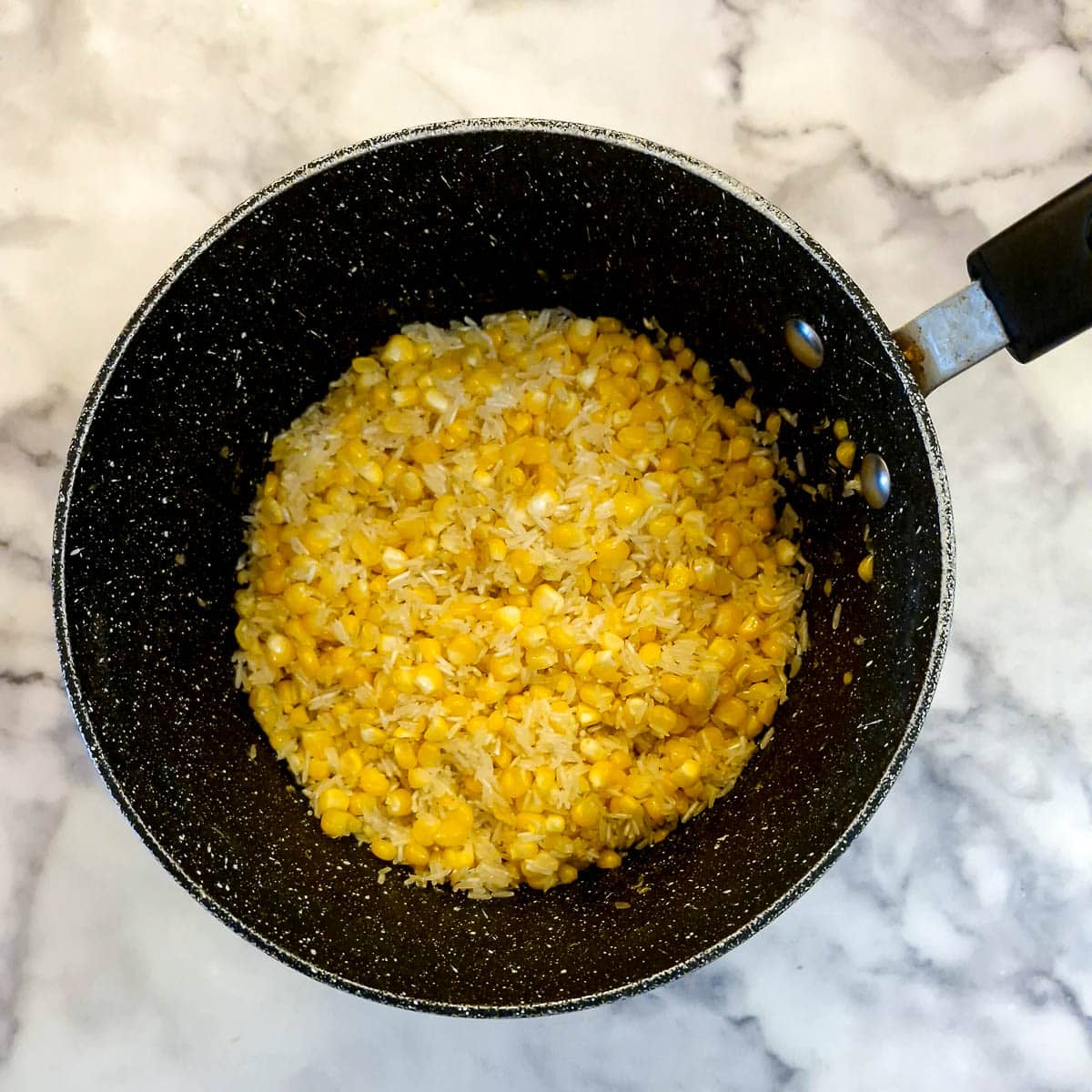 Corn kernels and raw basmati rice in melted butter in a saucepan.