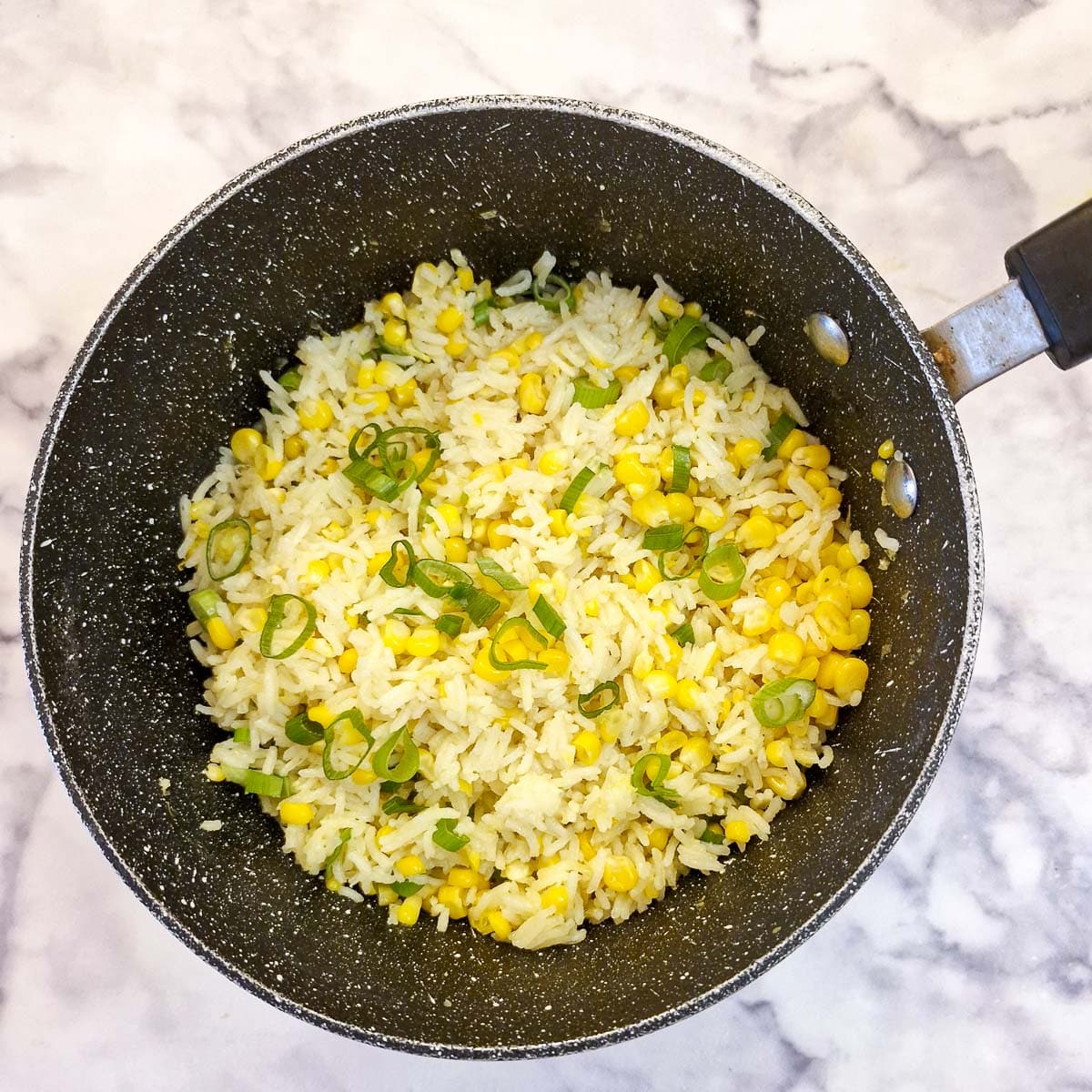 A saucepan of buttered corn and rice garnished with chopped green onions.