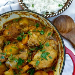Overhead view of a dish of chicken curry with a bowl of white rice.