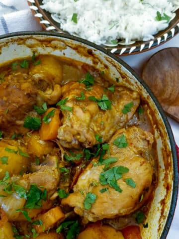 Overhead view of a dish of chicken curry with a bowl of white rice.