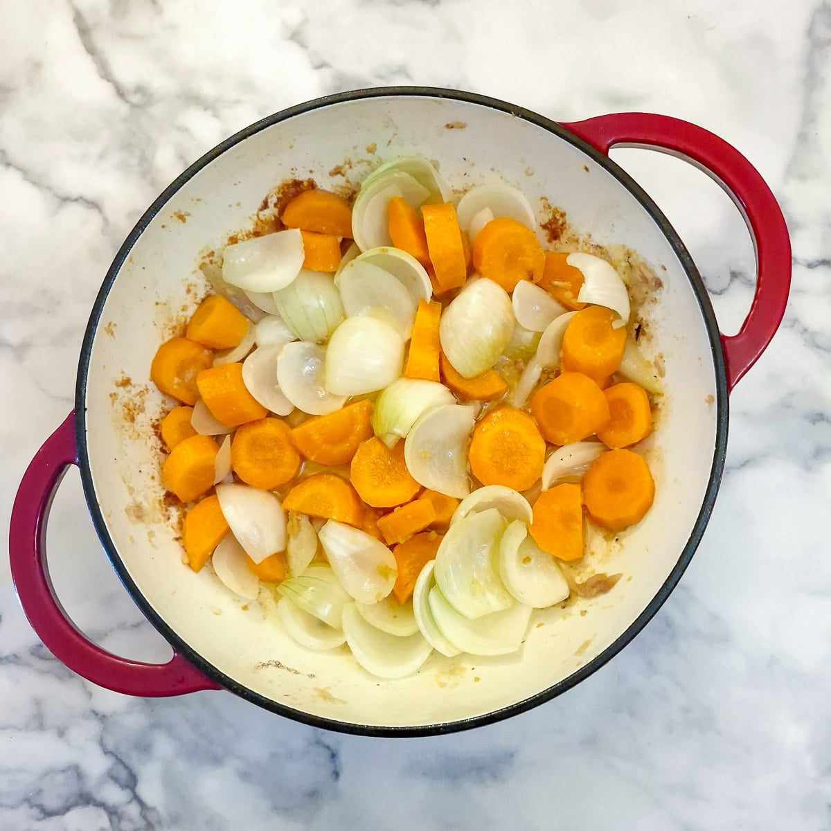 Onions and carrots softening in a frying pan.