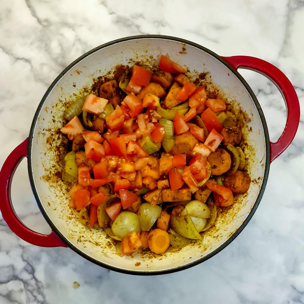 Chopped tomatoes softening with onions and carrots in a frying pan.