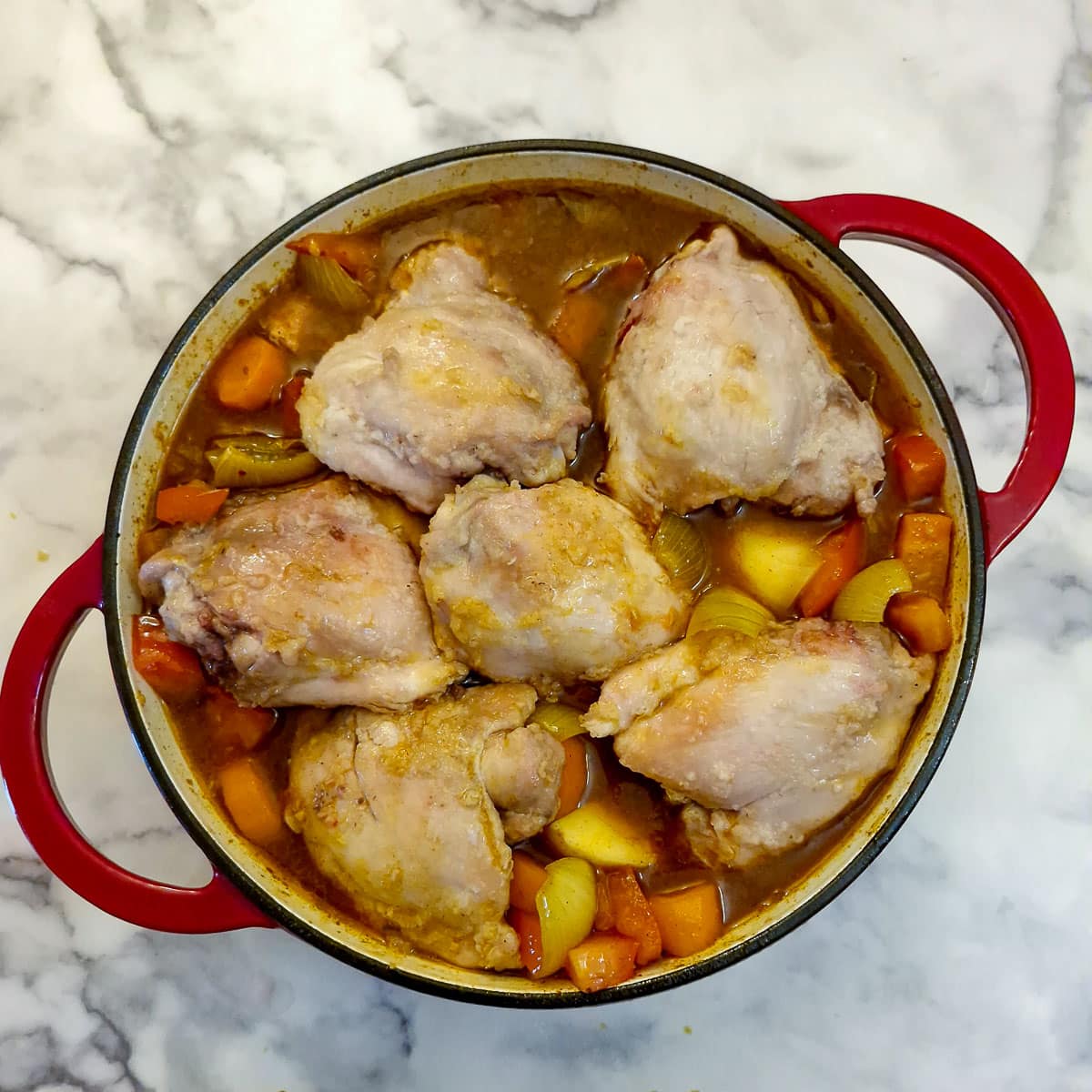 6 chicken thighs nestled into the curry sauce in a frying pan.