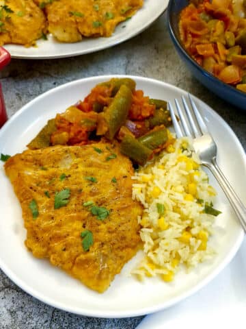 A piece of tempura-battered cod on a plate with rice and green beans.