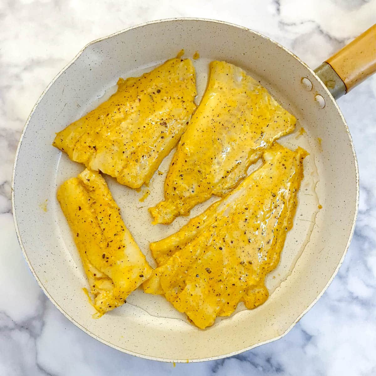 4 pieces of battered cod in a frying pan.