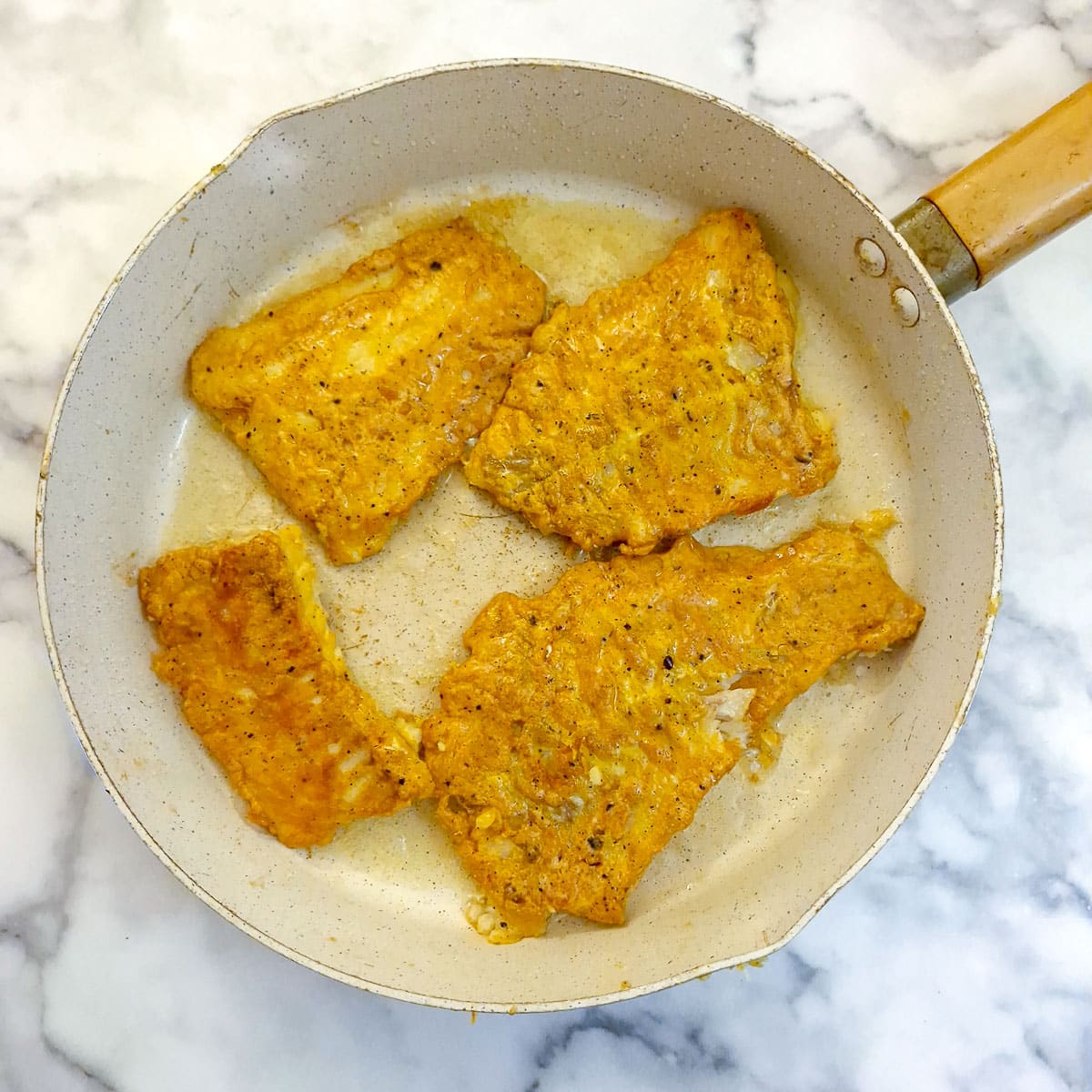 4 pieces of browned battered cod in a frying pan.