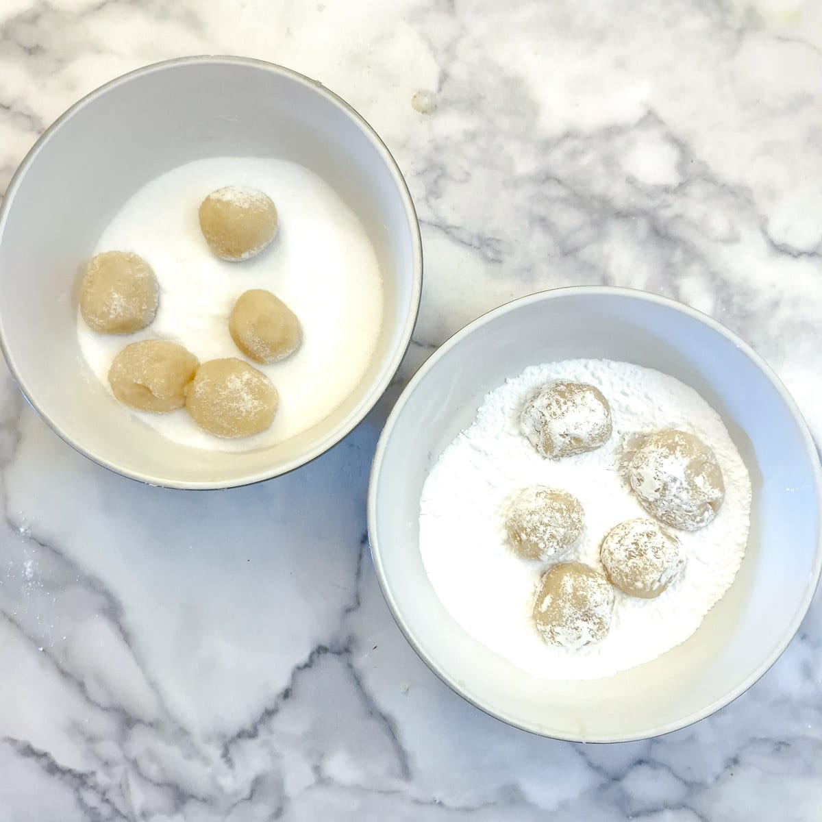 Two bowls, one with caster sugar and one with icing sugar, with balls of amaretti dough.