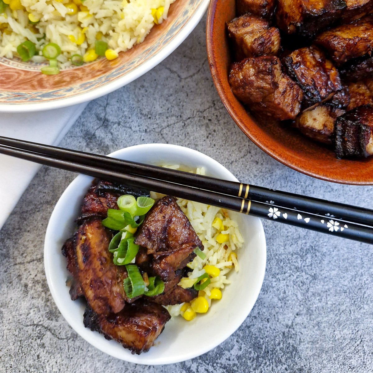 A small white bowl of pork belly bites with a dish of rice in the background.