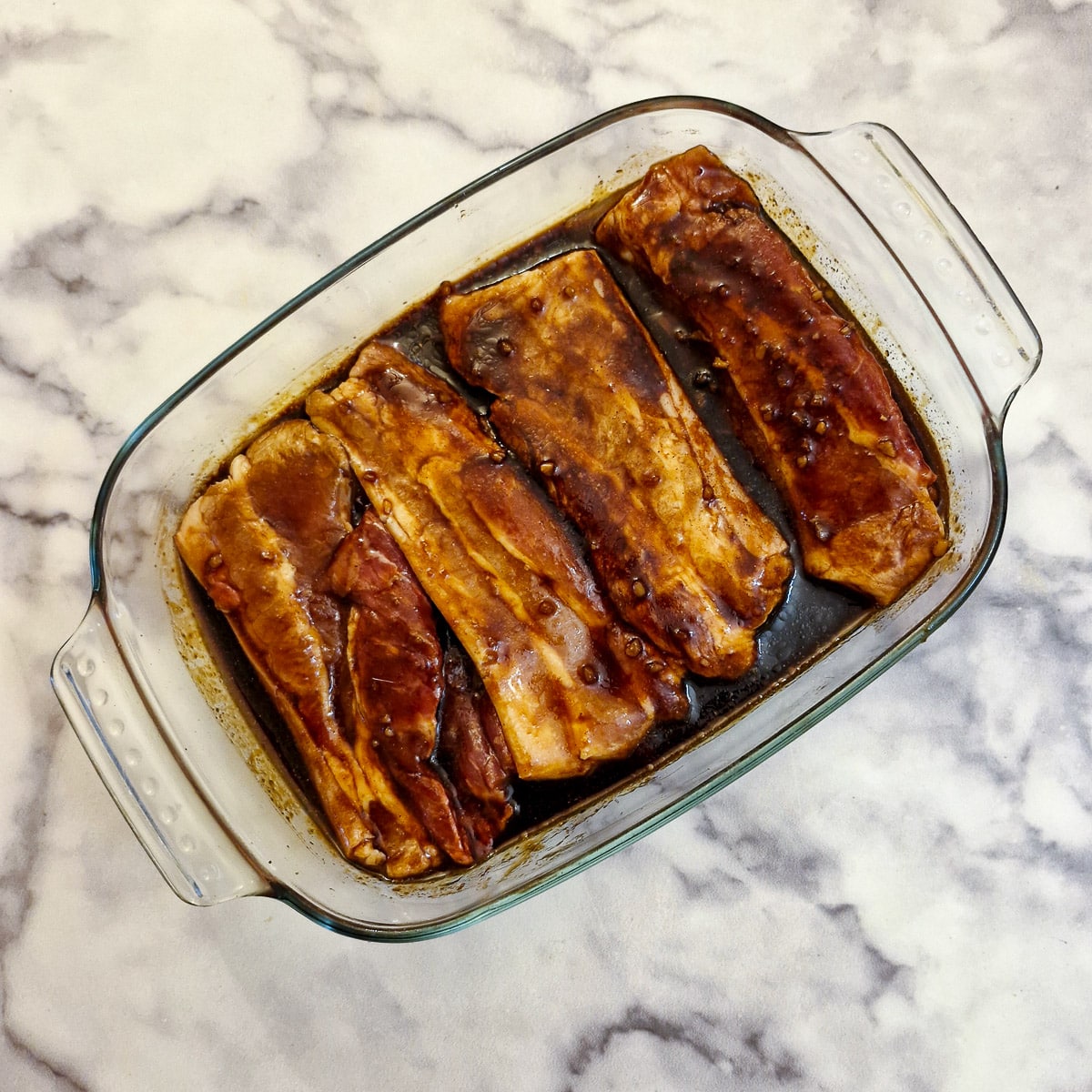 4 pork belly slices marinating in a glass dish.