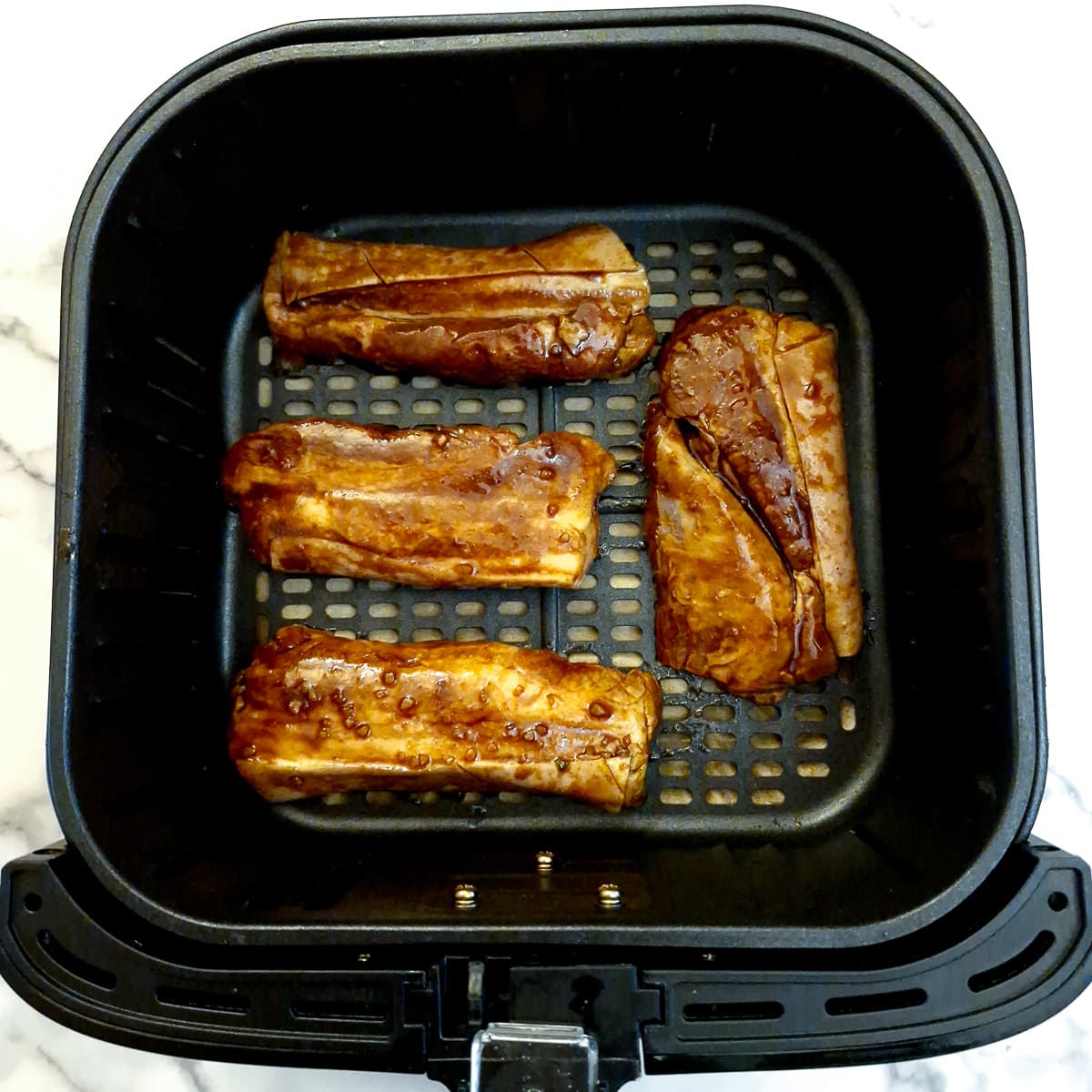 4 pork belly slices arranged in the basket of an air fryer.